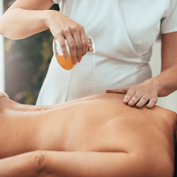 Warm oil being poured onto a woman's back as part of an Ayurveda Abhyanga massage