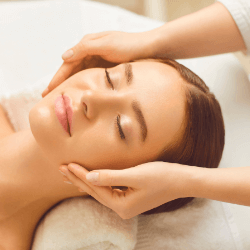 Woman with eyes closed laying on a massage bed receiving a head and face massage